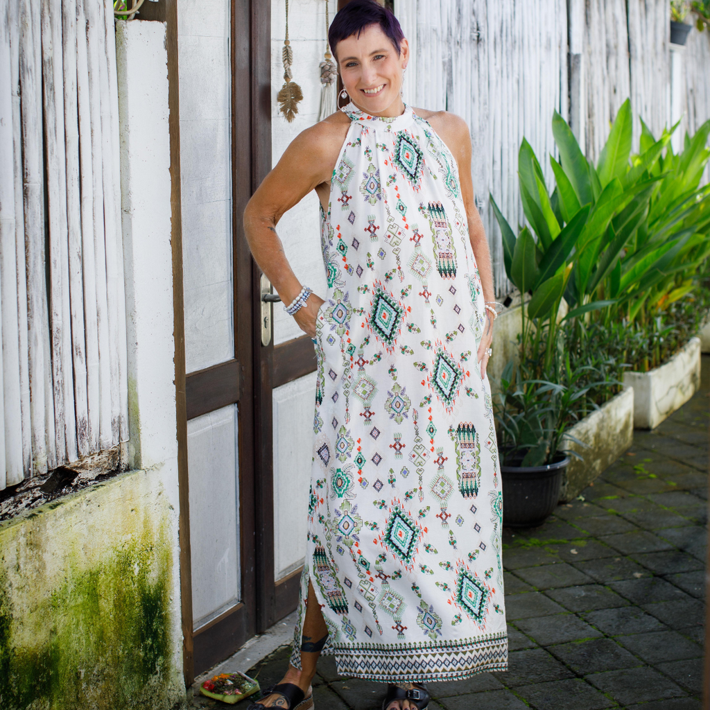 Woman in menopause wearing a patterned dress standing outdoors near a wooden door and plants.