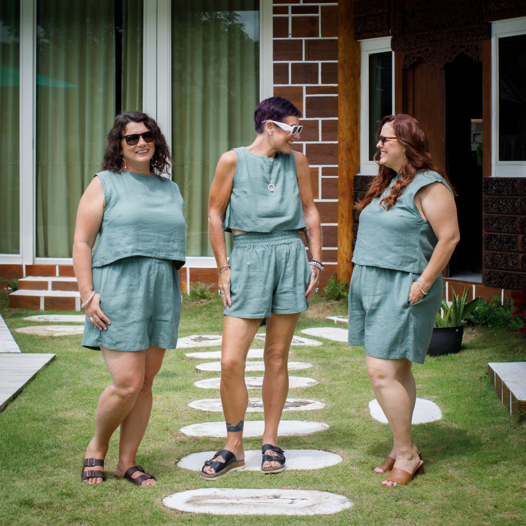 Three women in matching green outfits standing on a grassy area in front of a house.